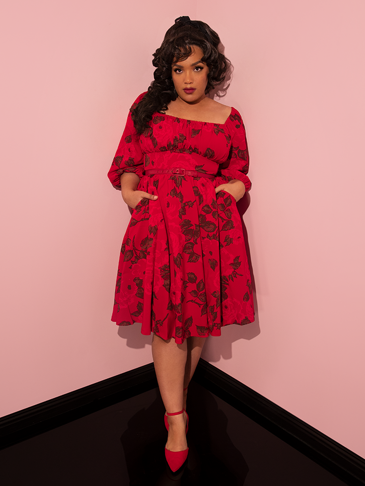 Ashleeta tucks her hands into the side pockets of her Vacation Dress in Vintage Red Rose Print from Vixen Clothing.