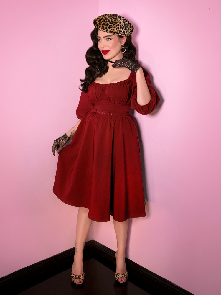 Full body shot of Micheline Pitt wearing the Vacation Dress in Ruby Red while also sporting black fishnet gloves and a leopard beret. 