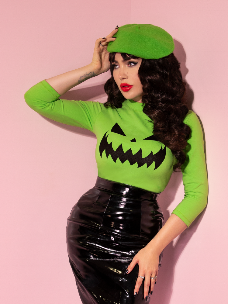 Posing with one hand on her black latex skirt and the other on her head, Micheline Pitt gives us a glimpse of the all-new Pumpkin King 3/4 Sleeve Top in Slime Green from Vixen Clothing.