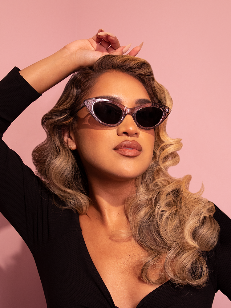 Model posing with one hand on top of her head while wearing the Fashion Doll Cat Eye Sunglasses in Spider Web.