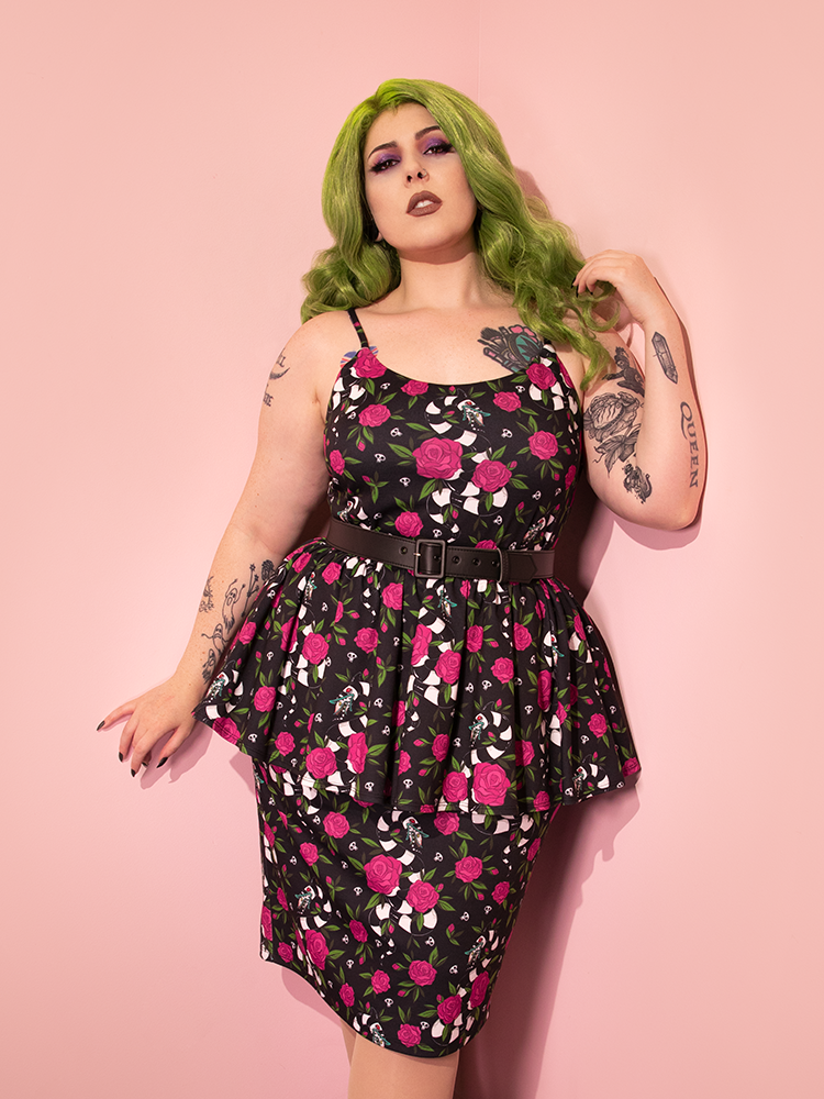 Green-haired model wearing the BEETLEJUICE™ Sandworm & Roses Peplum Wiggle Dress with adjust black faux leather belt.