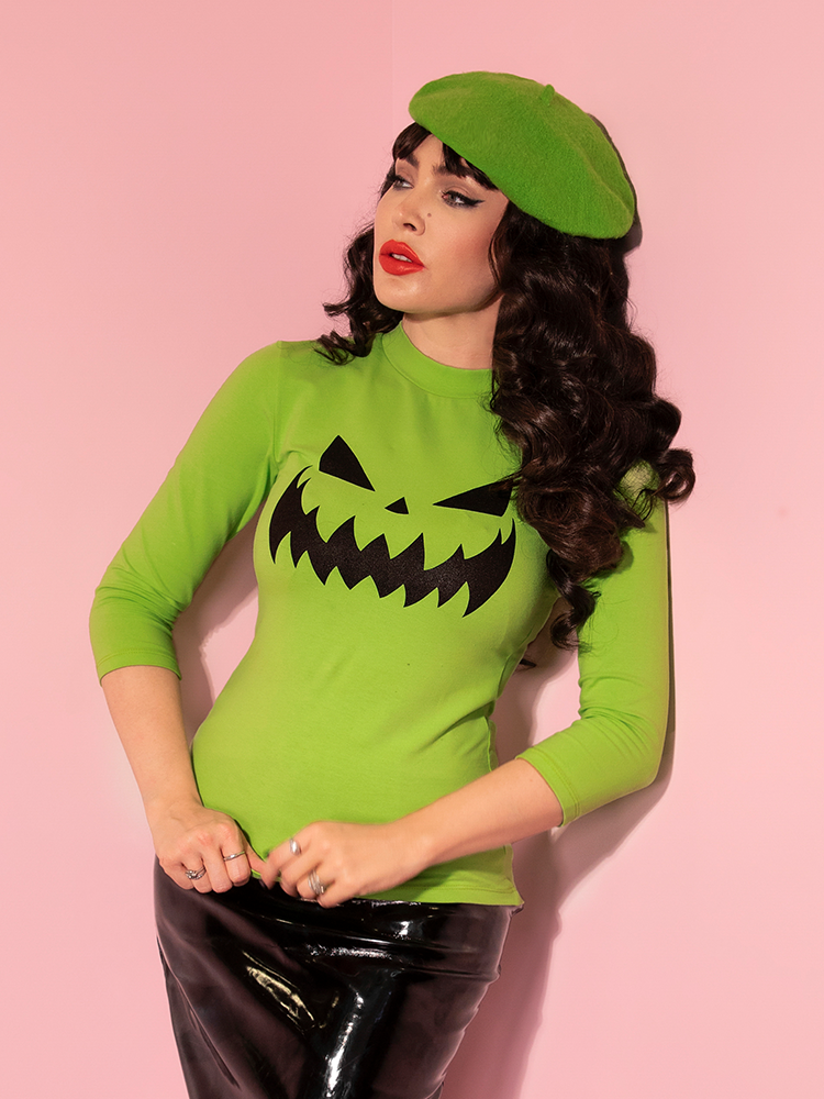 Gently tugging down on the front of her Pumpkin King 3/4 Sleeve Top in Slime Green, Micheline Pitt looks off-camera. 