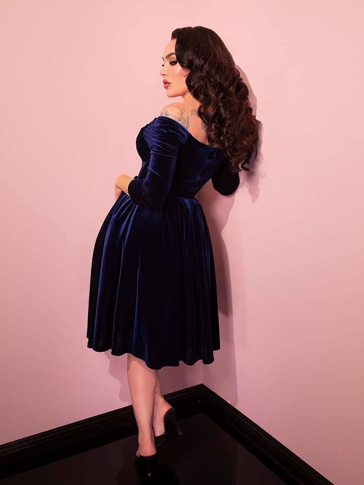 Micheline Pitt turned away from the camera to show off the back of the Starlet Swing Dress in Navy Velvet from retro dress brand Vixen Clothing.