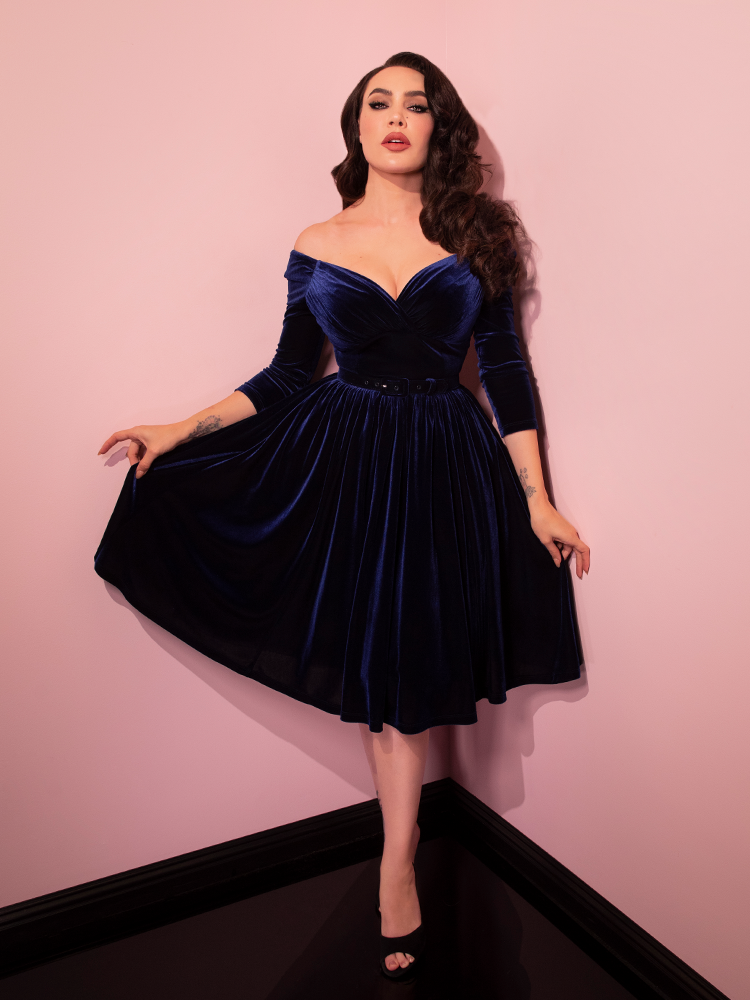 Micheline Pitt pulling out the sides of the Starlet Swing Dress in Navy Velvet from Vixen Clothing.