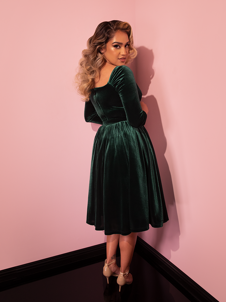 Model facing away from the camera gives us a glimpse of the back of the Starlet Swing Dress in Hunter Green Velvet