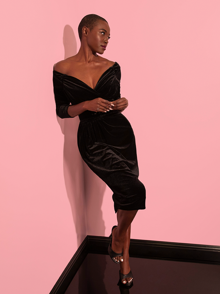 The female model looks gorgeous in the Starlet Wiggle Dress in Black Velvet from Vixen Clothing, embodying retro glamour with every pose.