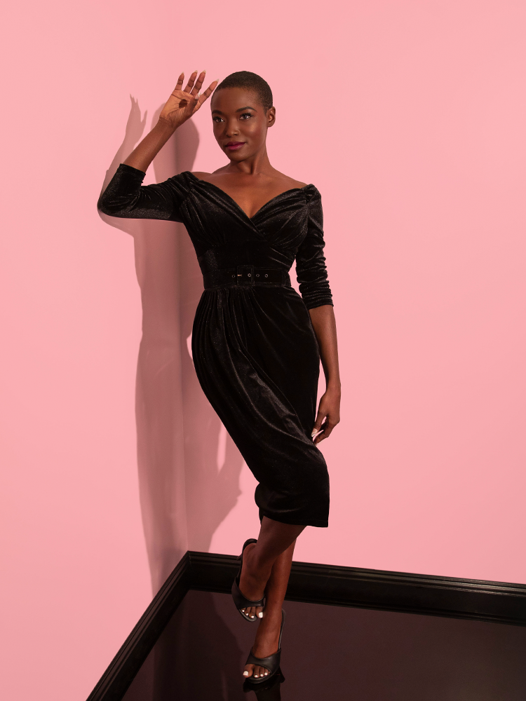 The female model is the epitome of retro chic in the Starlet Wiggle Dress in Black Velvet from Vixen Clothing, representing the brand with style.