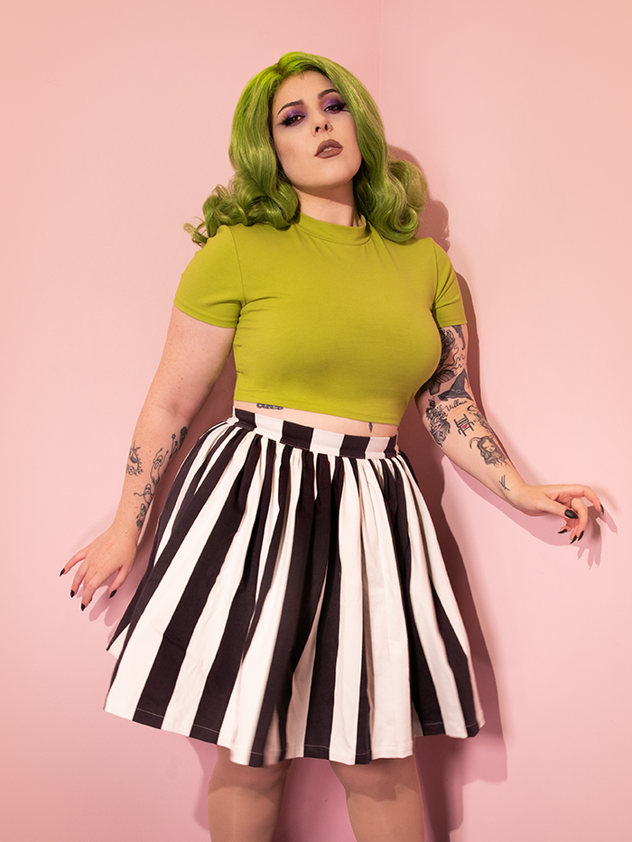 Green-haired female model wearing a green top with the Ghost Skater Skirt in Black & White Stripes from retro clothing brand Vixen Clothing.