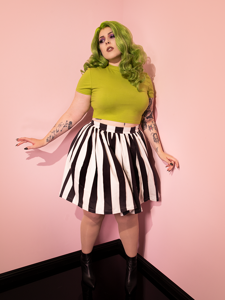 Full length image of female model in an all retro outfit including the Ghost Skater Skirt in Black & White Stripes and green top.