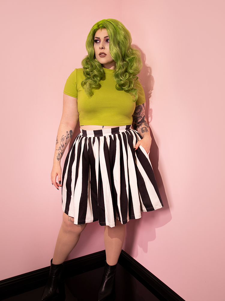 Model tucking her hand into the side pocket of the Ghost Skater Skirt in Black & White Stripes along with a short sleeve green top.