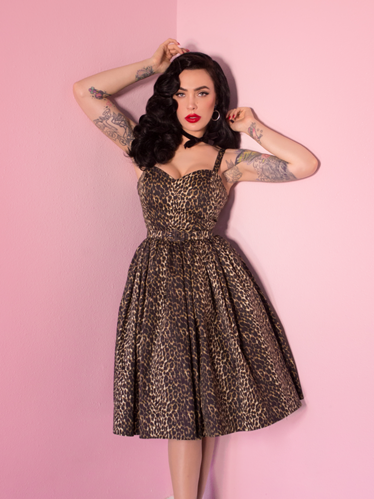 Micheline Pitt, raising her arms above her head, posing in a leopard print sweetheart swing dress.