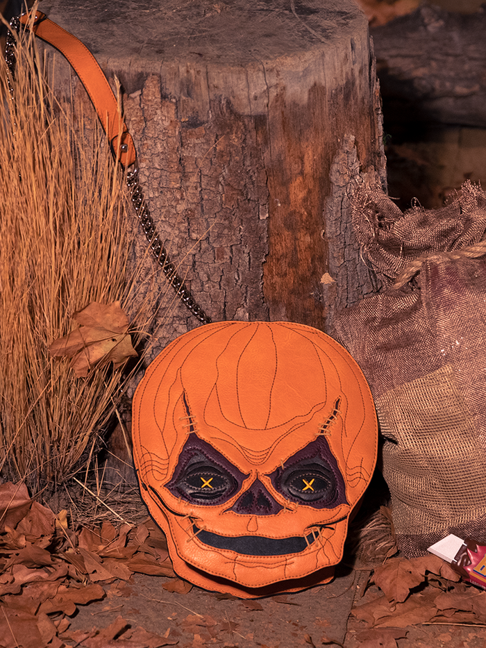The TRICK R TREAT™ Sam Crossbody Bag photographed in front of a tree stump and amongst dead leaves.