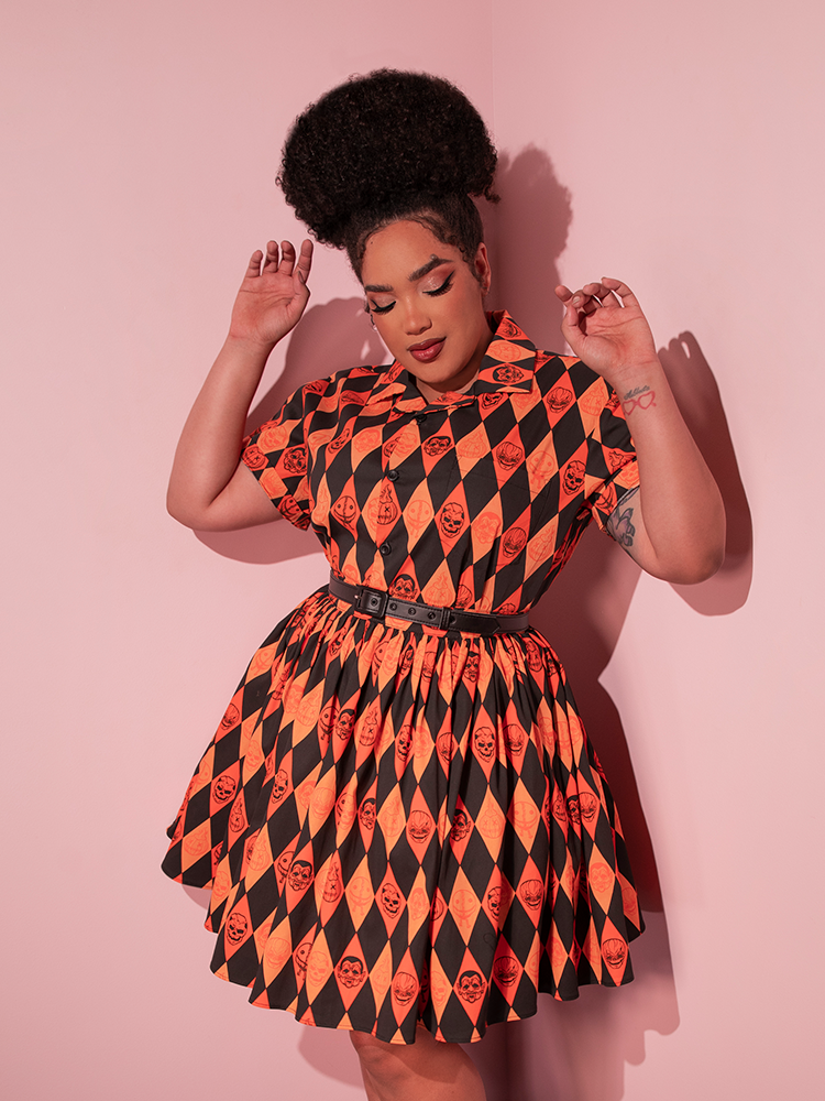 Model dancing around in her TRICK R TREAT™ Button Up Shirt in Halloween Harlequin Print that she's paired with a matching skirt.