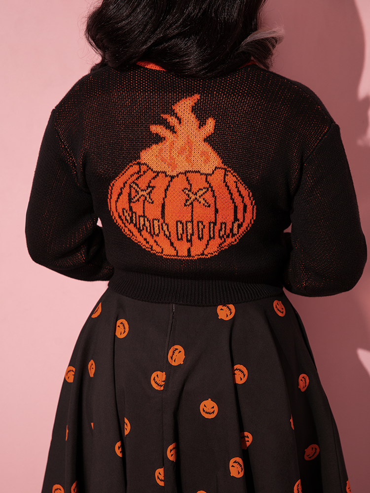 Close up of the flaming pumpkin design on the back of the TRICK R TREAT™ Flaming Pumpkin Cropped Knit Jacket as worn by Vixen model.