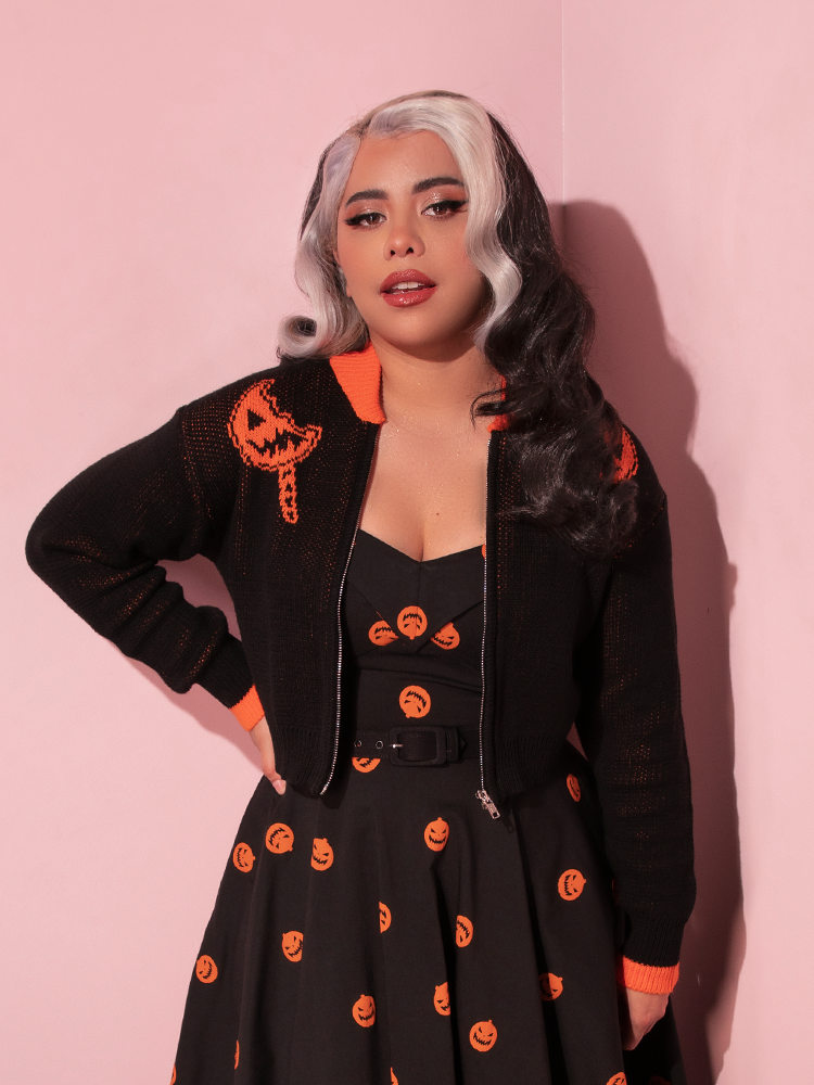 Model posing with her hand on her hip wearing the TRICK R TREAT™ Flaming Pumpkin Cropped Knit Jacket.