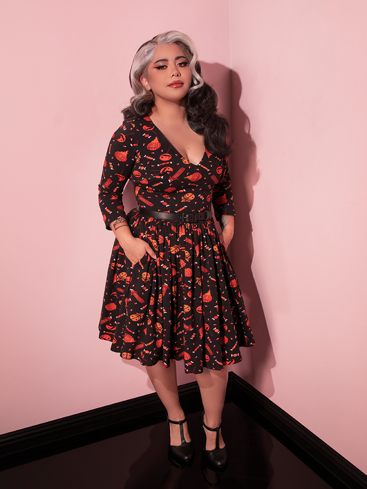Model tucking her hands into the pockets of the TRICK R TREAT™ Deadly Swing Dress in Candy Corn Novelty Print from retro dress brand Vixen Clothing.