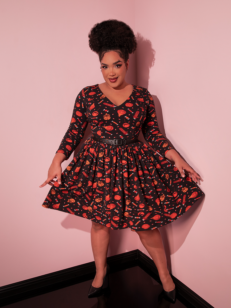 Model tugs out on the sides of the skirt on the TRICK R TREAT™ Deadly Swing Dress in Candy Corn Novelty Print to show off the spooky Halloween design.