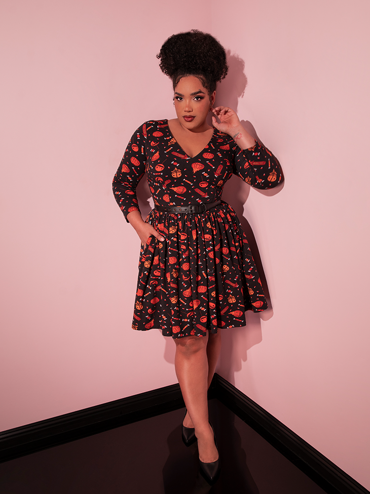Full length shot of female model standing in the corner of a room wearing the TRICK R TREAT™ Deadly Swing Dress in Candy Corn Novelty Print.