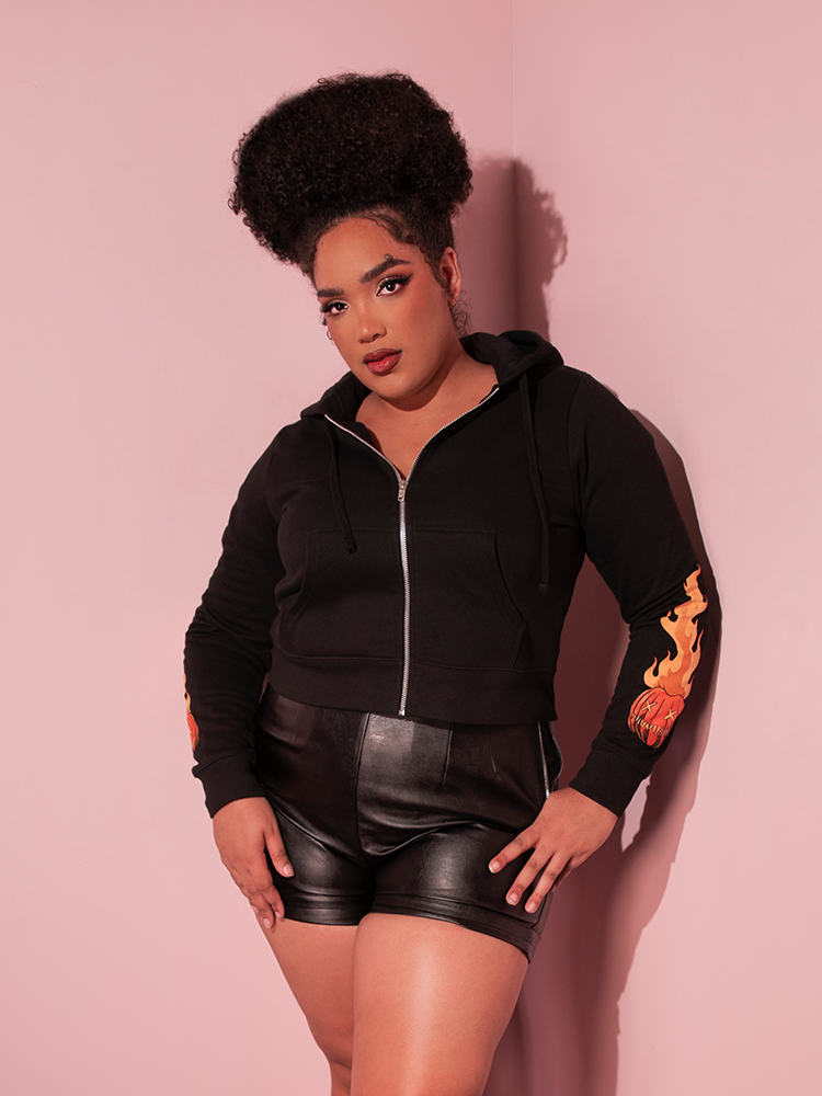 Model, photographed from the knee up, wearing the TRICK R TREAT™ Sam Cropped Hoodie over a pair of vegan leather shorts. 