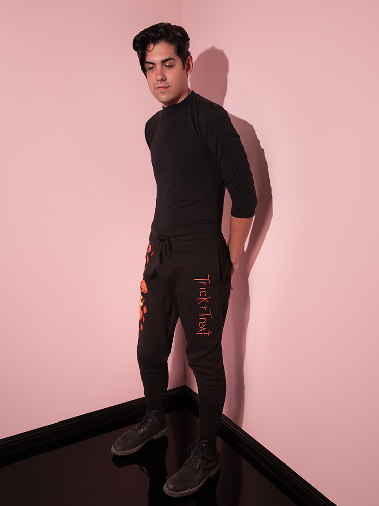 Male model turned to the side whiel wearing the TRICK R TREAT™ Jack O' Lantern Sweatpants and a black long sleeve shirt.