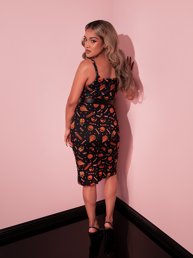 Model facing away from the camera, looks back over her shoulder at it while wearing the TRICK R TREAT™ Peplum Wiggle Dress in Candy Corn Novelty Print.