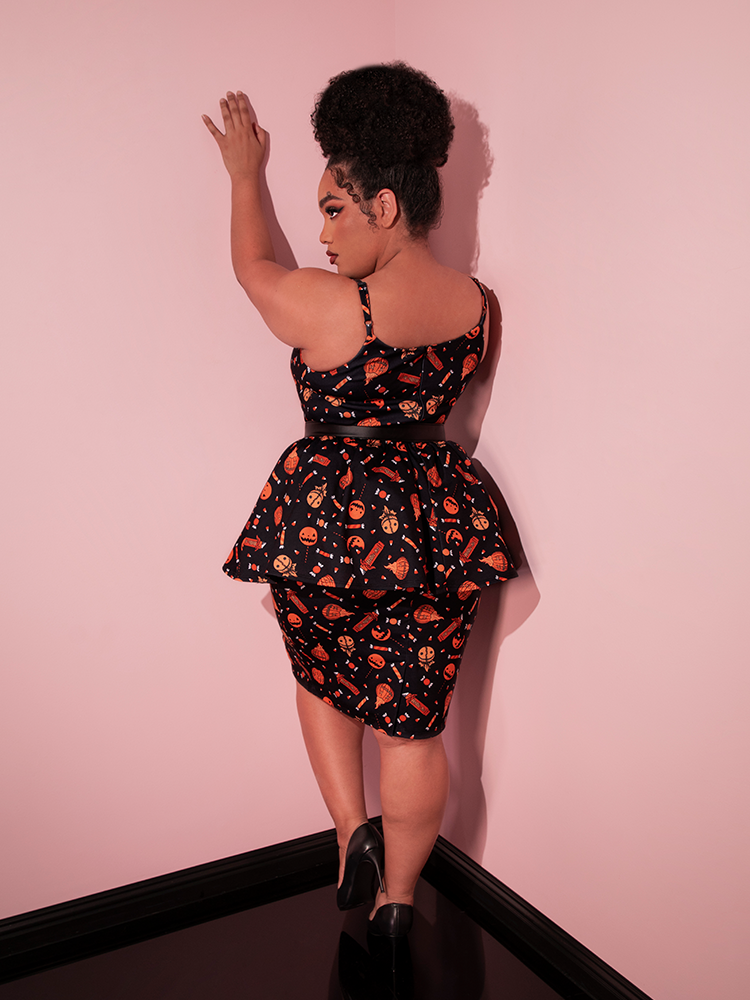 Model facing away from the camera to show off the back of the TRICK R TREAT™ Peplum Wiggle Dress in Candy Corn Novelty Print from retro clothing brand Vixen Clothing.