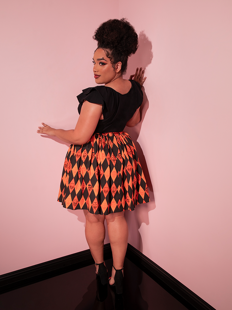 Model turned away from the camera to show off the back of the TRICK R TREAT™ Skater Skirt in Halloween Harlequin Print from Vixen Clothing.
