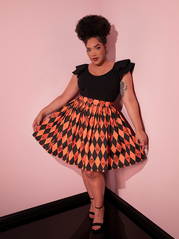 Model pulling out the sides of the skirt on the TRICK R TREAT™ Skater Skirt in Halloween Harlequin Print to show off the retro spooky print.