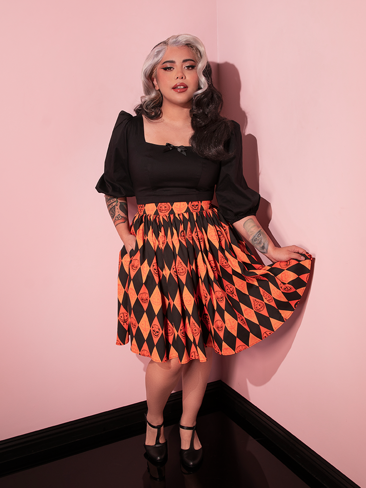 Female model pulls out the skirt on the TRICK R TREAT™ Skater Skirt in Halloween Harlequin Print to show off the retro style print on this vintage inspired skirt.