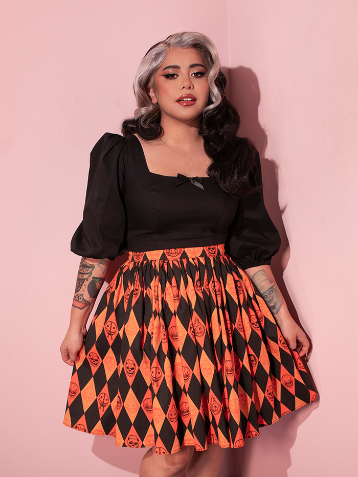The TRICK R TREAT™ Skater Skirt in Halloween Harlequin Print paired with a low cut black long sleeve retro top worn by vintage model - all items available from Vixen Clothing.