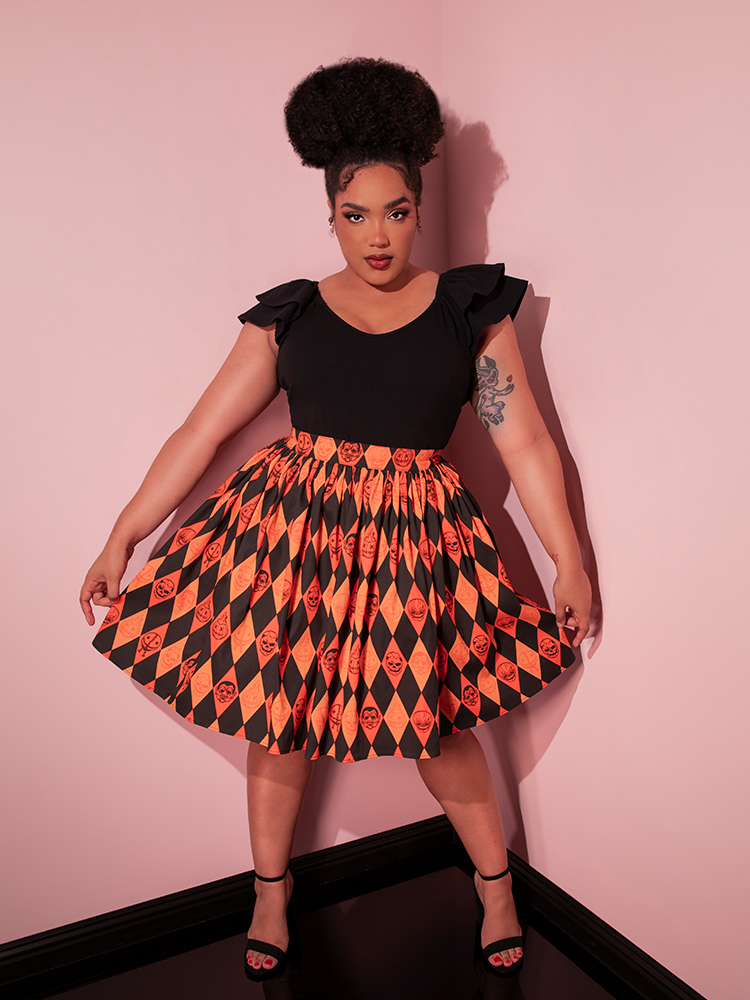 The TRICK R TREAT™ Skater Skirt in Halloween Harlequin Print worn by female model paired with a black low cut top. 