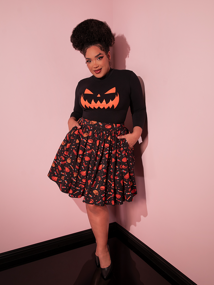 Female model struts towards the camera with her hands tucked into the pockets of the TRICK R TREAT™ Skater Skirt in Candy Corn Novelty Print.