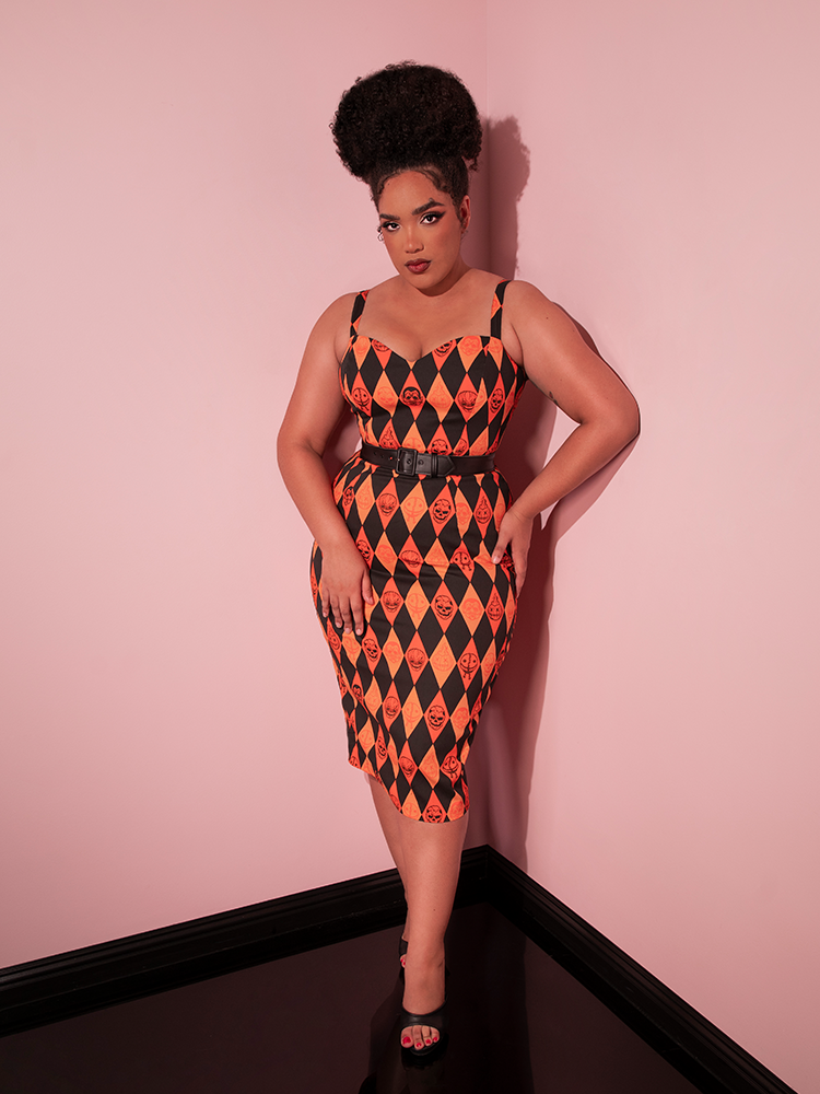 Model hold a serious gaze on her face while looking at the camera while wearing the TRICK R TREAT™ Sweetheart Wiggle Dress in Halloween Harlequin Print.