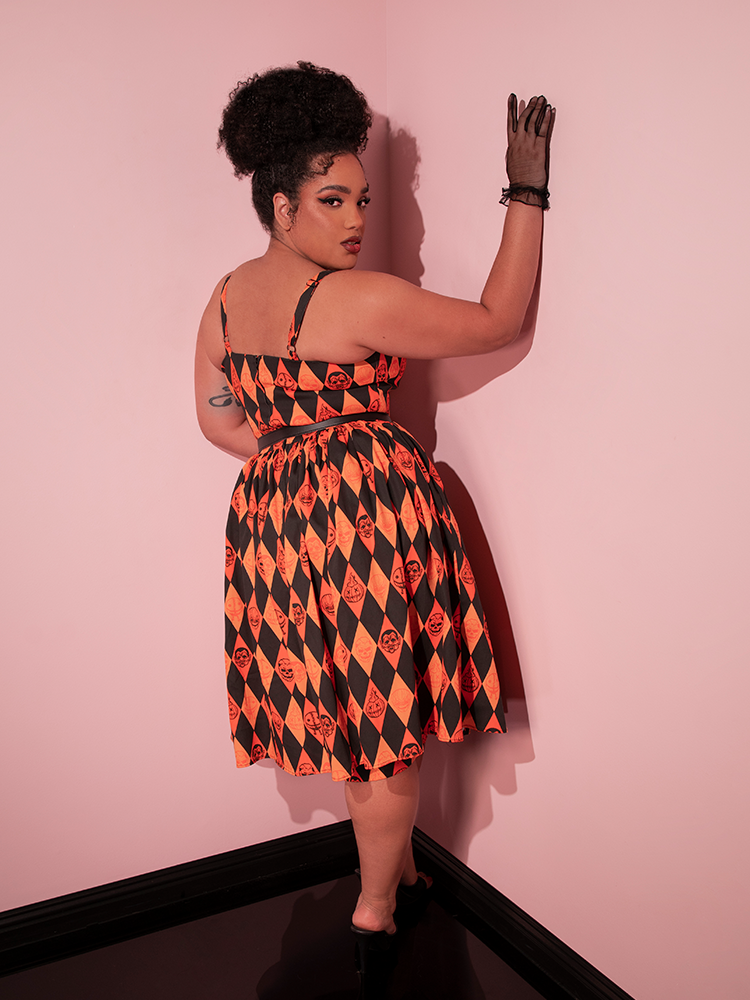 Model facing away from the camera while wearing the TRICK R TREAT™ Sweetheart Swing Dress in Halloween Harlequin Print to show off the back of the retro style dress.