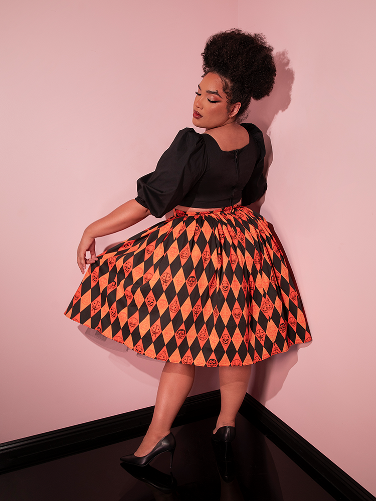 Model turned away from the camera while holding out the side of the TRICK R TREAT™ Swing Skirt in Halloween Harlequin Print to give a clear view of the Halloween inspired print.