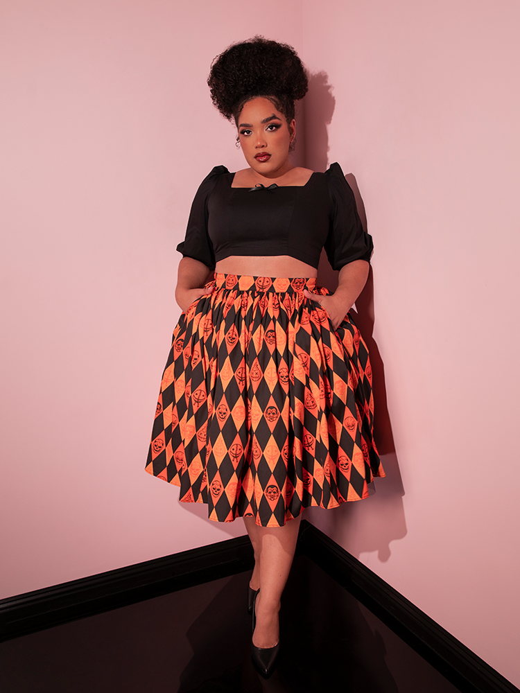 Female model tucking her hands into the side pockets of the TRICK R TREAT™ Swing Skirt in Halloween Harlequin Print along with a retro style black top.