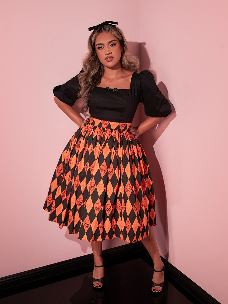 Model posing with her hands on her hips while wearing the TRICK R TREAT™ Swing Skirt in Halloween Harlequin Print from retro clothing brand Vixen Clothing.