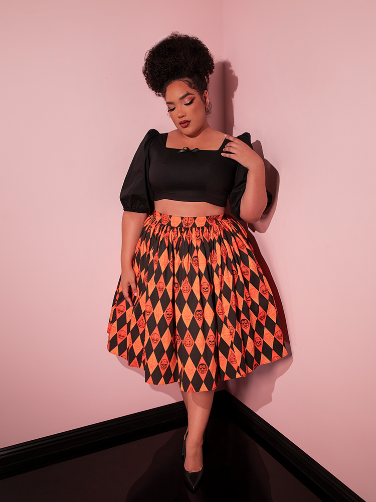 Model looking down at the floor while wearing the TRICK R TREAT™ Swing Skirt in Halloween Harlequin Print paired with a black top with flowy sleeves to make the perfect retro style outfit.