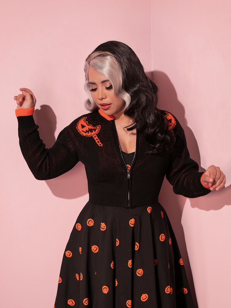 Model dancing around while wearing the TRICK R TREAT™ Flaming Pumpkin Cropped Knit Jacket.