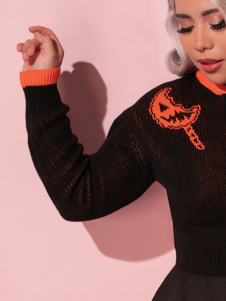The sleeve of the TRICK R TREAT™ Flaming Pumpkin Cropped Knit Jacket as worn by female Vixen model.