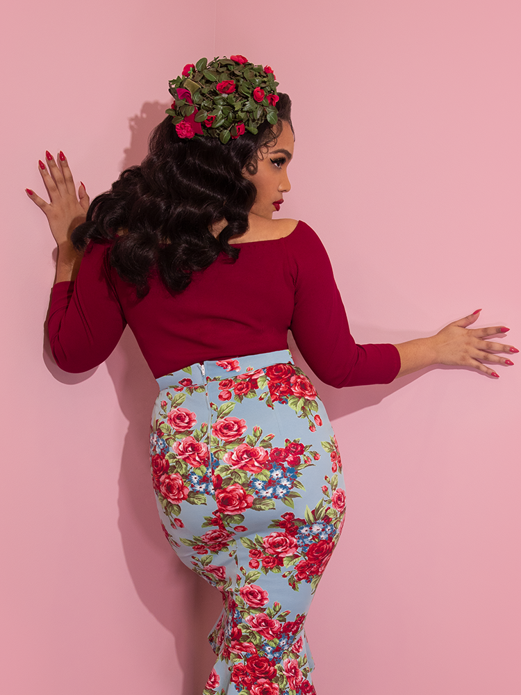 A back view of Ashleeta modeling the tie me up top in red by Vixen Clothing paired with a blue floral skirt and floral pillbox hat.