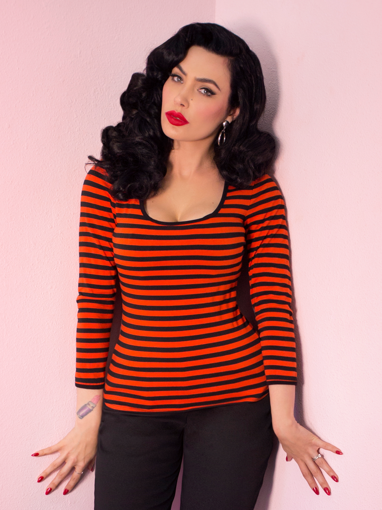 A closeup photo of Micheline Pitt modeling the Troublemaker top in orange and black stripes untucked by Vixen Clothing.