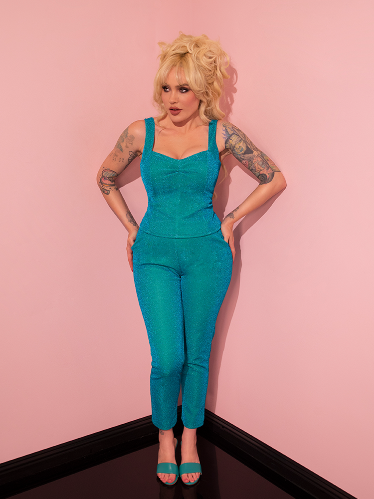 Radiating beauty and confidence, the model charms in her retro ensemble, highlighting the playful and sexy Cigarette Pants in Turquoise Lurex from Vixen Clothing.