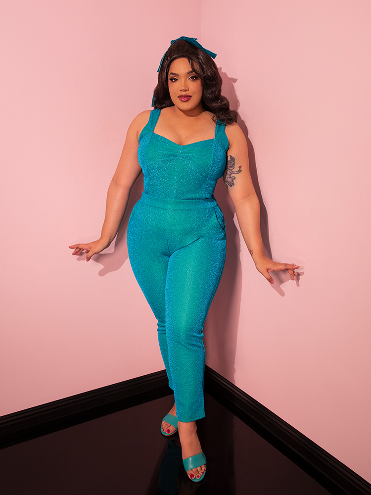 Captivating onlookers with her striking pose, the gorgeous model showcases the Turquoise Lurex Cigarette Pants from Vixen Clothing's retro line, exuding both fun and sexiness.