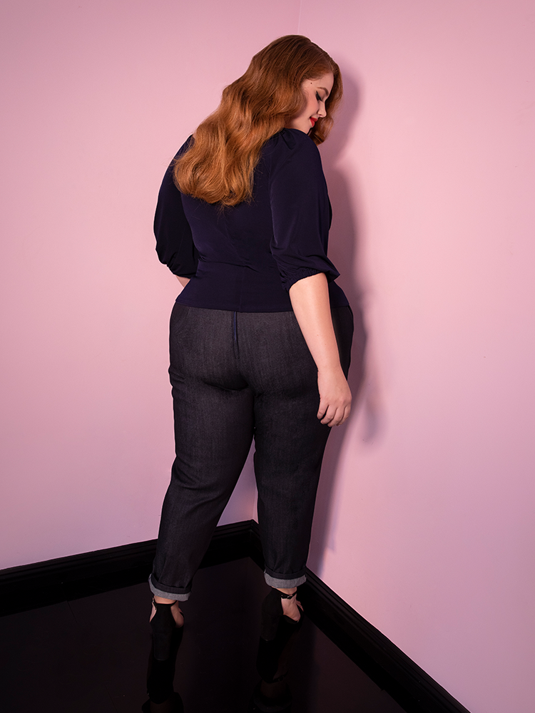 Bree turned away from the camera models the cigarette pants in denim from Vixen Clothing paired with a navy top.