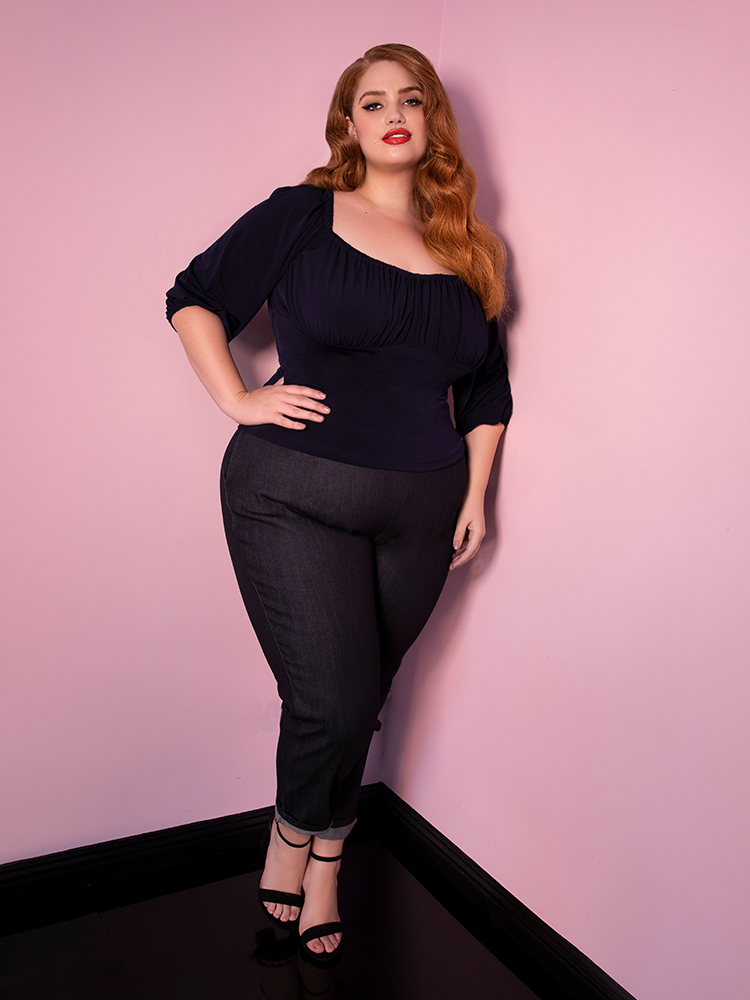 Bree with her hand on her hip models the cigarette pants in denim from Vixen Clothing paired with a navy top.
