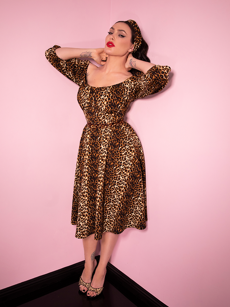 Full body length picture of Micheline Pitt in an all leopard vintage inspired outfit - featuring a leopard print headband, dress and heeled shoes.