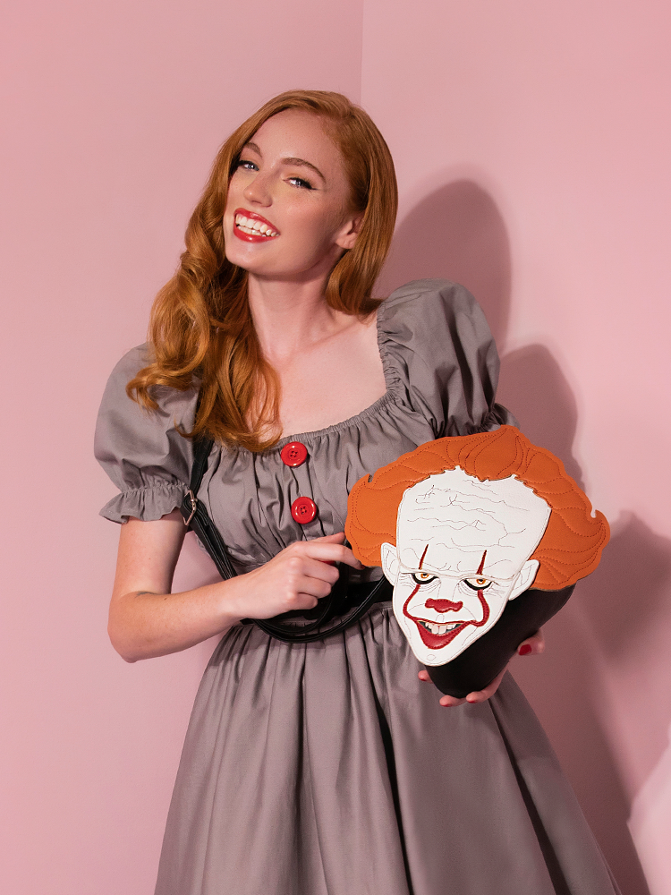 Model Emily flashes a big smile while holding her Pennywise clown crossbody bag by Vixen Clothing.