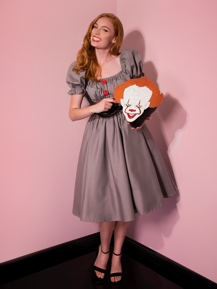 Wearing a big smile while holding a Pennywise bag, Emily models the Pennywise babydoll dress by Vixen Clothing.
