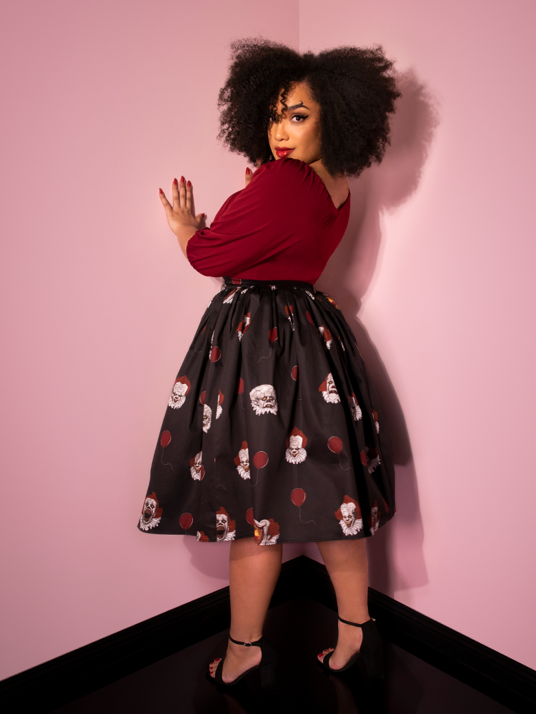 Turned away from the camera and looking over her shoulder, Ashleeta models the Pennywise swing skirt in black by Vixen Clothing.